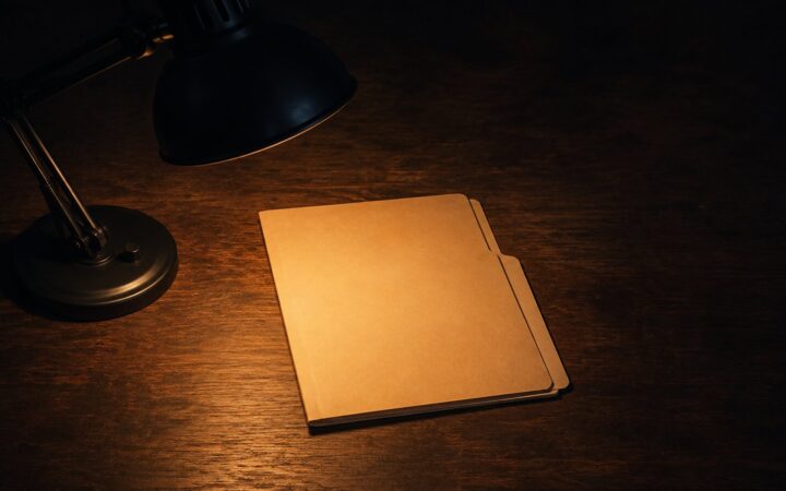 A manila folder lit by a desk lamp on a dark wooden desk, representing a prepared case for asking for a raise