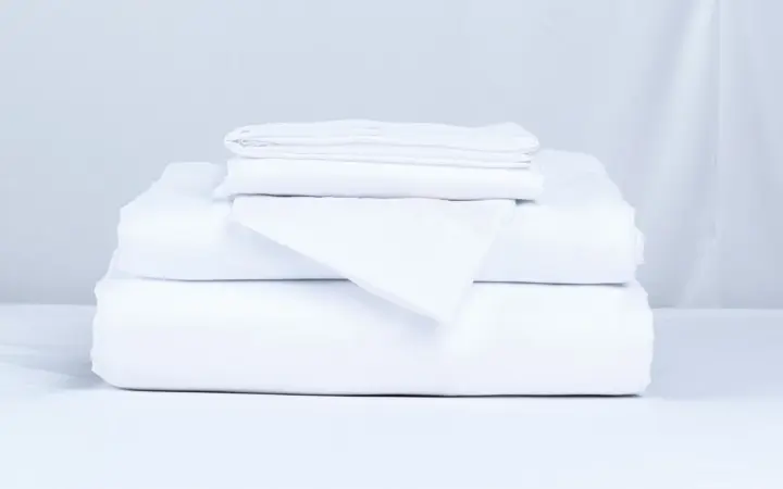 A stack of folded white bed linen on a plain pale surface