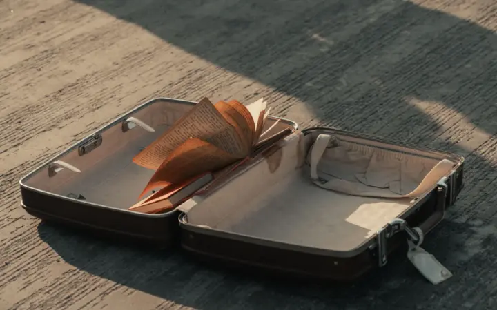 An open, almost empty suitcase on concrete in low sunlight, with one book inside