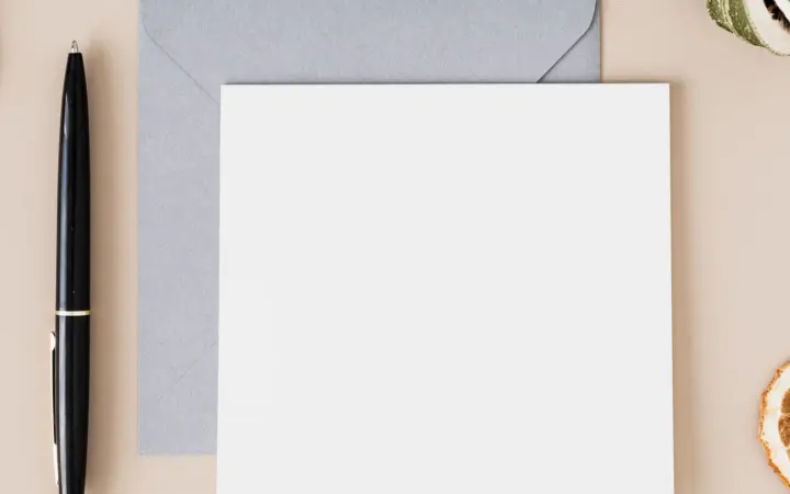 A blank white notecard resting on a grey envelope beside a pen, seen from above